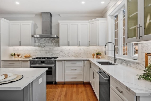 kitchen featuring sink, appliances with stainless steel finishes, white cabinetry, light stone counters, and wall chimney exhaust hood