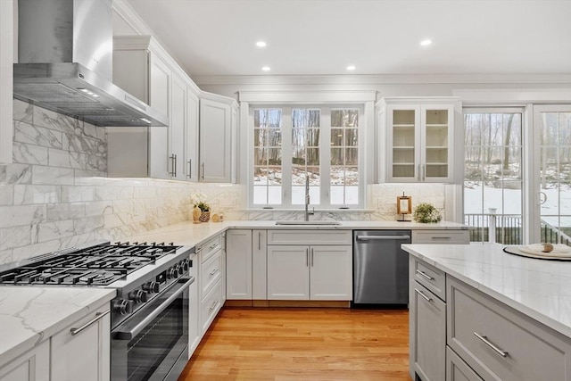 kitchen featuring sink, stainless steel appliances, light stone countertops, white cabinets, and wall chimney exhaust hood