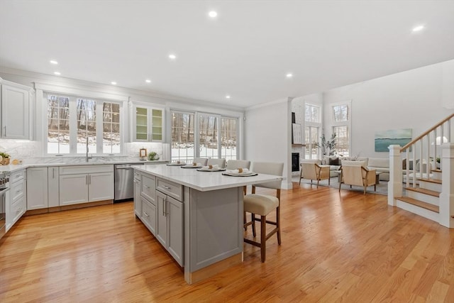 kitchen featuring a kitchen island, a breakfast bar, decorative backsplash, stainless steel dishwasher, and light hardwood / wood-style floors