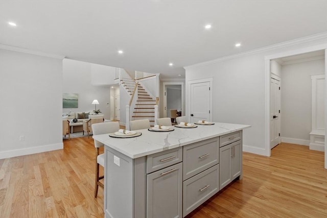 kitchen with gray cabinets, a kitchen island, a breakfast bar, light stone countertops, and light hardwood / wood-style flooring