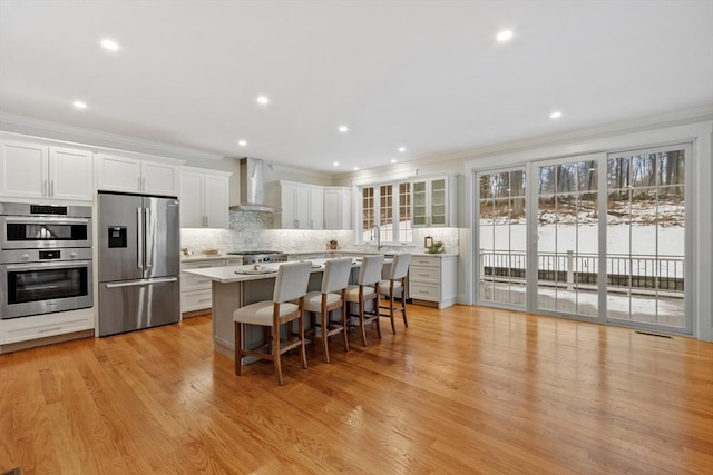 kitchen featuring wall chimney range hood, a breakfast bar area, white cabinetry, stainless steel appliances, and a kitchen island