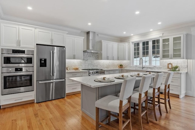 kitchen with a breakfast bar, a center island, wall chimney range hood, stainless steel appliances, and white cabinets