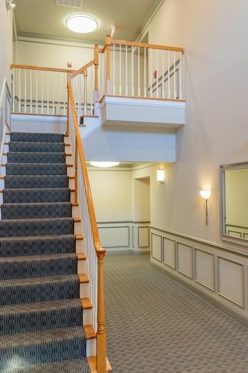 stairway with visible vents, a wainscoted wall, a high ceiling, carpet floors, and a decorative wall