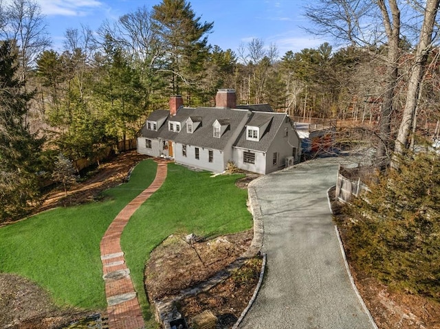 view of front of home featuring a chimney, a wooded view, and a front yard