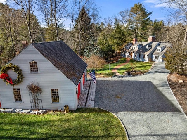 view of side of property with a shingled roof, gravel driveway, and a yard