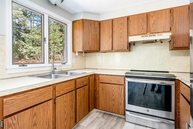 kitchen with a sink, stainless steel electric stove, light countertops, under cabinet range hood, and backsplash