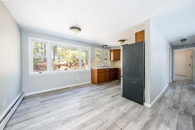 kitchen featuring brown cabinets, freestanding refrigerator, baseboard heating, light countertops, and light wood-style floors