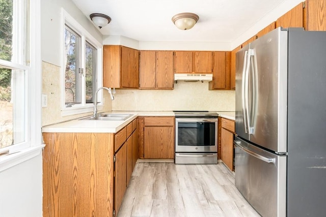 kitchen featuring brown cabinets, stainless steel appliances, light countertops, under cabinet range hood, and a sink