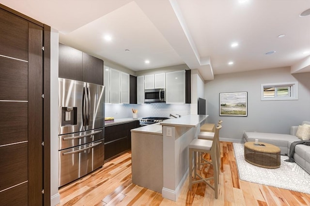 kitchen with kitchen peninsula, light hardwood / wood-style floors, a kitchen bar, decorative backsplash, and appliances with stainless steel finishes