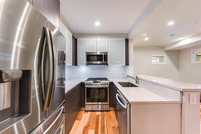 kitchen with backsplash, sink, light hardwood / wood-style floors, kitchen peninsula, and stainless steel appliances