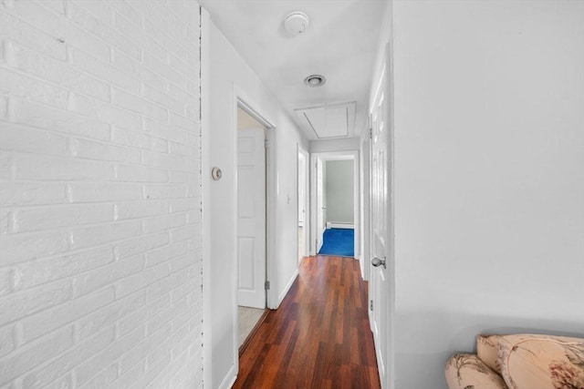 hallway with brick wall, attic access, baseboards, and dark wood-type flooring