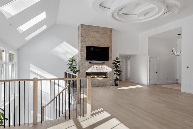 living area with a skylight, baseboards, a stone fireplace, light wood-type flooring, and high vaulted ceiling