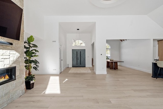 entrance foyer featuring an inviting chandelier, a stone fireplace, high vaulted ceiling, light wood-type flooring, and baseboards