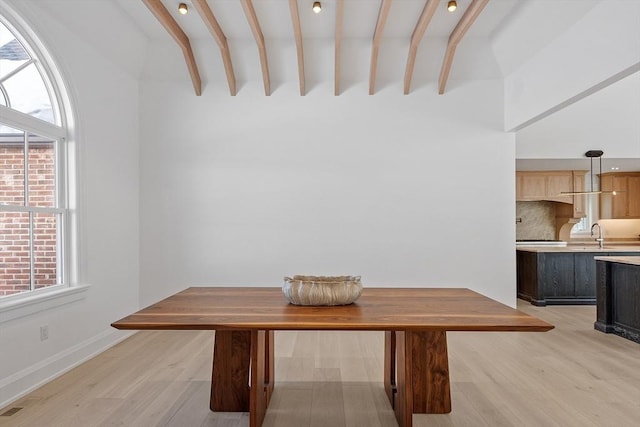 unfurnished dining area with light wood-type flooring, a sink, baseboards, and beam ceiling