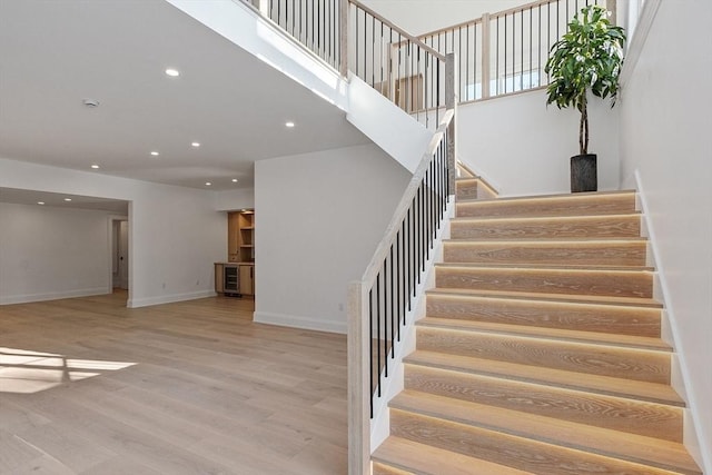 stairway with a high ceiling, baseboards, wood finished floors, and recessed lighting