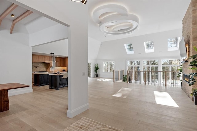 living room with baseboards, a high ceiling, a skylight, and light wood-style floors