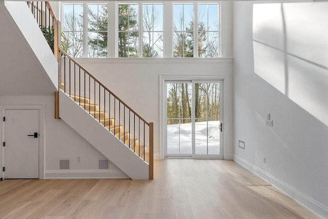 doorway to outside featuring light wood-type flooring, visible vents, a high ceiling, and stairs