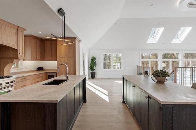 kitchen featuring a spacious island, lofted ceiling with skylight, light countertops, stainless steel stove, and a sink