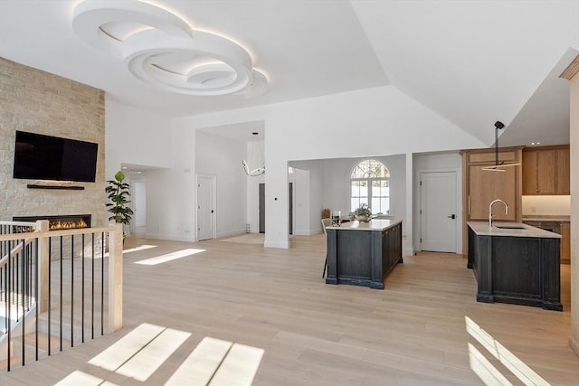 kitchen featuring light countertops, open floor plan, a kitchen island with sink, and a stone fireplace