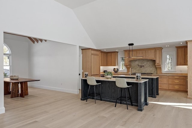 kitchen with a breakfast bar, a center island with sink, light countertops, hanging light fixtures, and light wood-style flooring