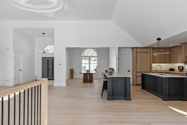 kitchen with decorative light fixtures, a center island with sink, light countertops, light wood-style floors, and a sink