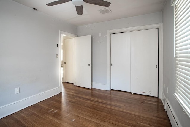 unfurnished bedroom with ceiling fan, dark hardwood / wood-style floors, baseboard heating, and a closet