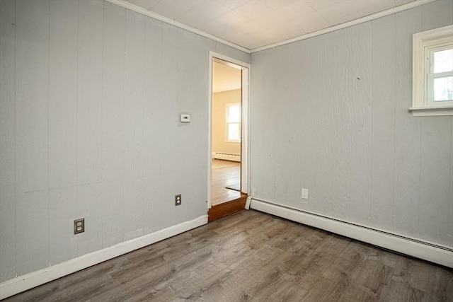 spare room with light hardwood / wood-style floors, ornamental molding, baseboard heating, and a wealth of natural light