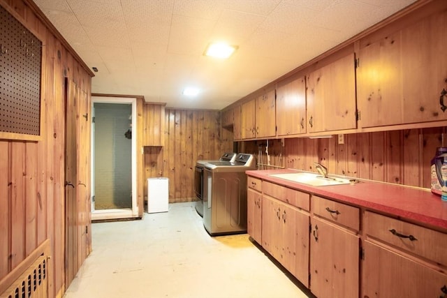 clothes washing area featuring cabinets, washer and dryer, wooden walls, and sink