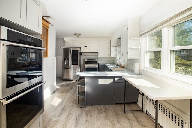 kitchen featuring white cabinetry, radiator heating unit, sink, light hardwood / wood-style flooring, and appliances with stainless steel finishes