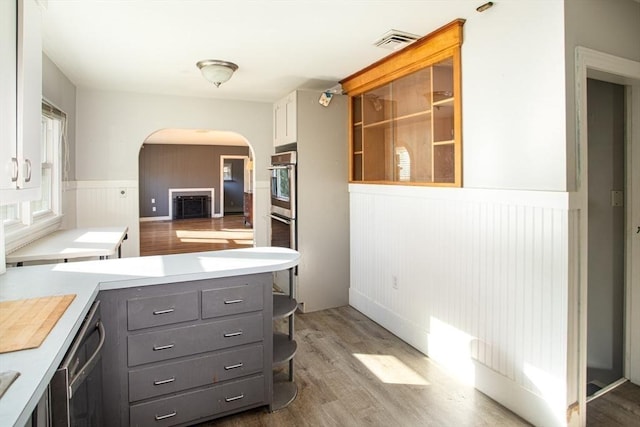 kitchen with stainless steel dishwasher, multiple ovens, dark wood-type flooring, gray cabinets, and white cabinetry