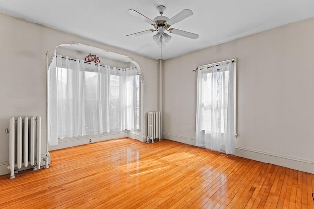 empty room featuring a ceiling fan, radiator, and hardwood / wood-style flooring