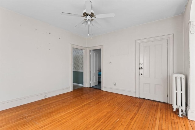 empty room featuring radiator, light wood-style floors, baseboards, and a ceiling fan