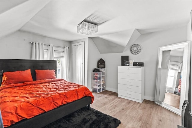 bedroom with light wood-style floors, baseboards, vaulted ceiling, and a closet