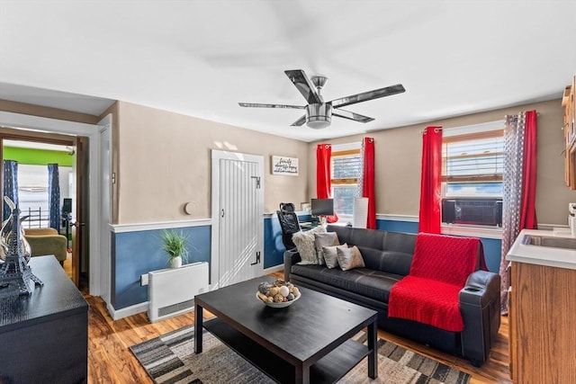 living area with light wood-type flooring, cooling unit, a ceiling fan, and baseboards