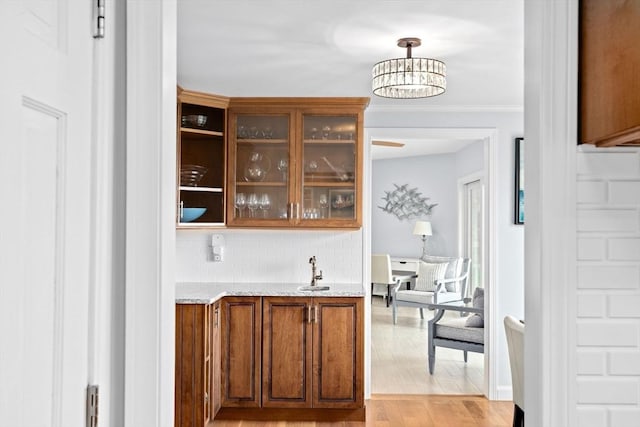 bar with tasteful backsplash, a sink, hanging light fixtures, an inviting chandelier, and light wood finished floors