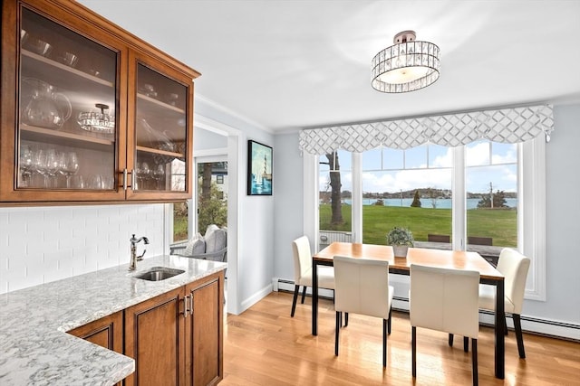 dining space featuring light wood finished floors, a water view, wet bar, baseboard heating, and crown molding