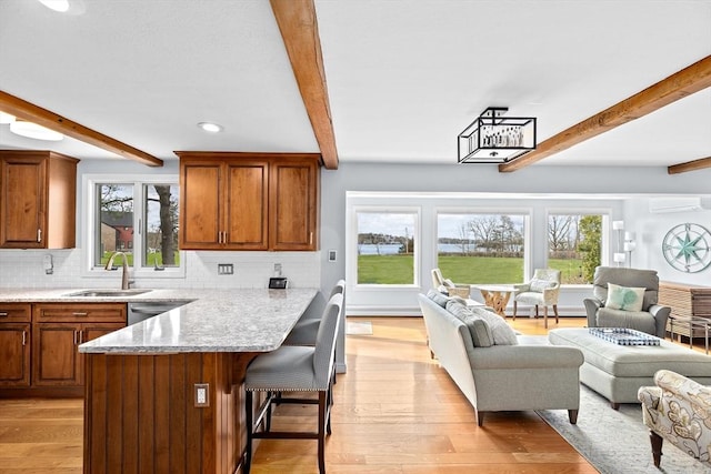 kitchen with open floor plan, beam ceiling, light wood finished floors, and a breakfast bar area