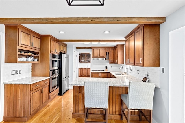kitchen with brown cabinets, stainless steel appliances, a sink, a peninsula, and light wood-style flooring