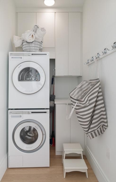 laundry room featuring stacked washing maching and dryer and light hardwood / wood-style floors