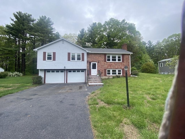 bi-level home featuring driveway, a chimney, an attached garage, a front yard, and view of wooded area