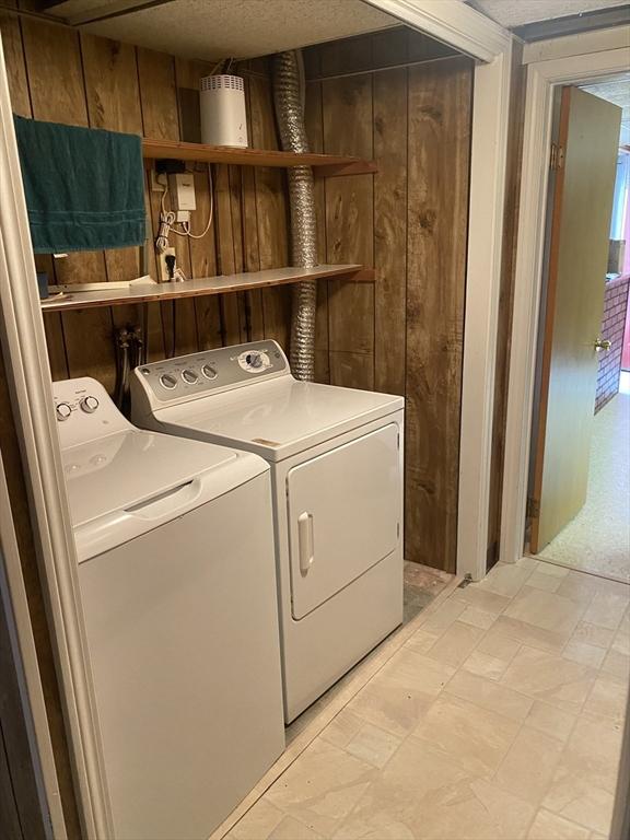 laundry room with washer and clothes dryer, light floors, and wooden walls