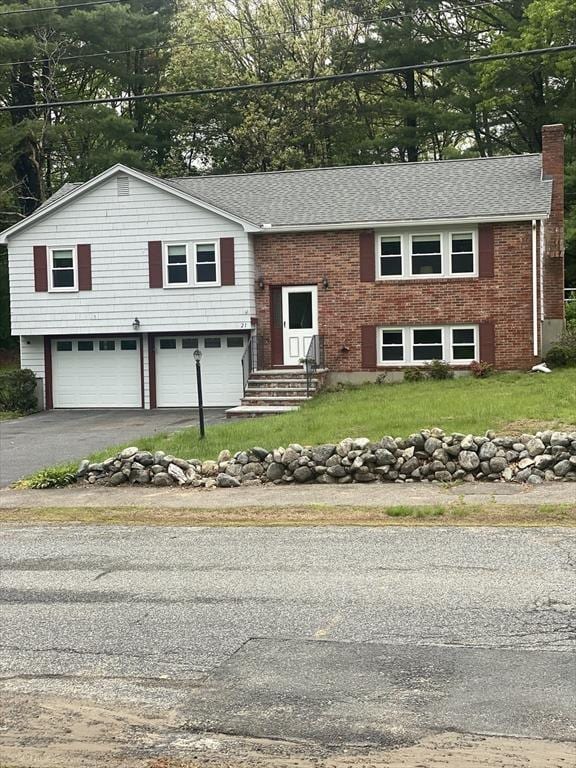bi-level home featuring a garage, asphalt driveway, a chimney, and brick siding