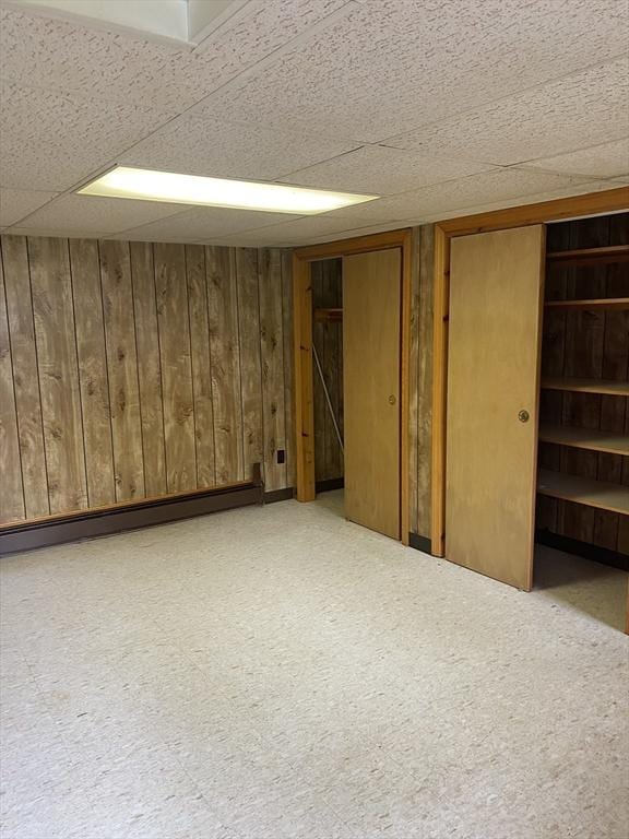 finished below grade area with a drop ceiling, a baseboard heating unit, and wooden walls