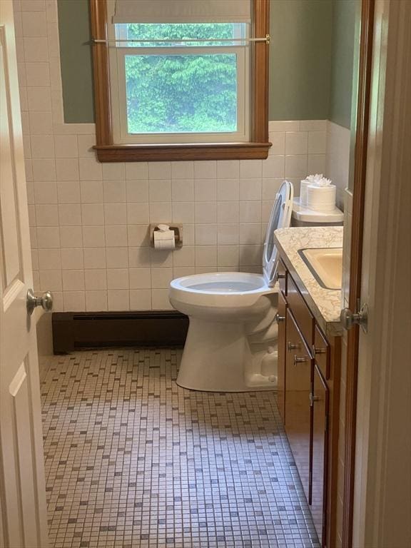 half bath featuring tile walls, a baseboard heating unit, toilet, and vanity