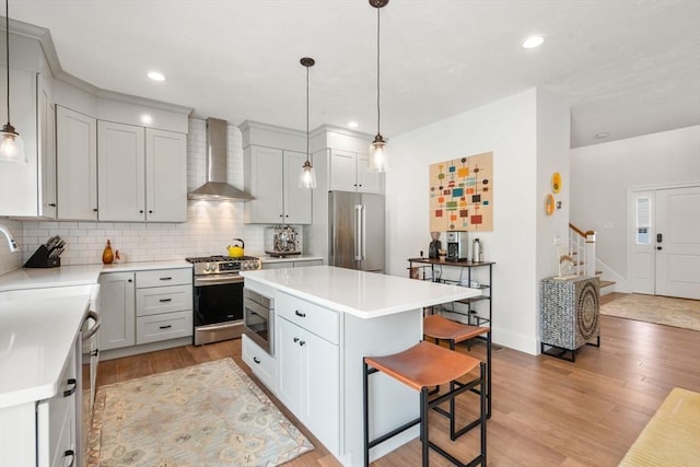 34 Sumner St Unit 34, Norfolk, MA 02056 - kitchen featuring stainless steel appliances, wall chimney exhaust hood, a kitchen bar, light wood-style floors, and tasteful backsplash