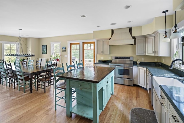 kitchen with stainless steel range with electric cooktop, a center island, light wood-type flooring, premium range hood, and pendant lighting