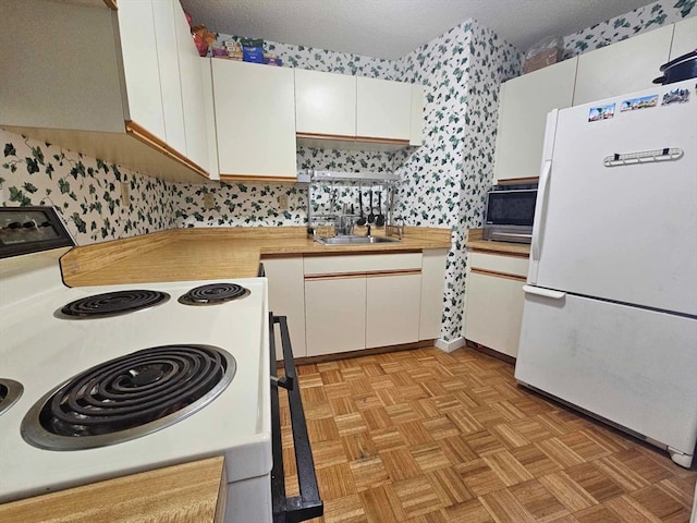 kitchen with light parquet flooring, white appliances, white cabinetry, and a textured ceiling