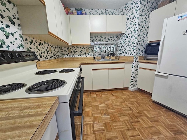 kitchen with white cabinets, white appliances, light parquet floors, and sink