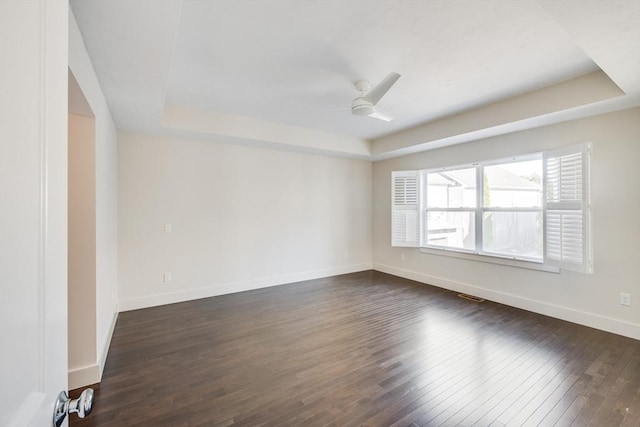 empty room with visible vents, baseboards, dark wood finished floors, a ceiling fan, and a tray ceiling