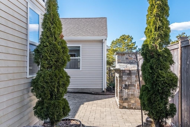 view of side of home featuring a shingled roof, fence, and a patio